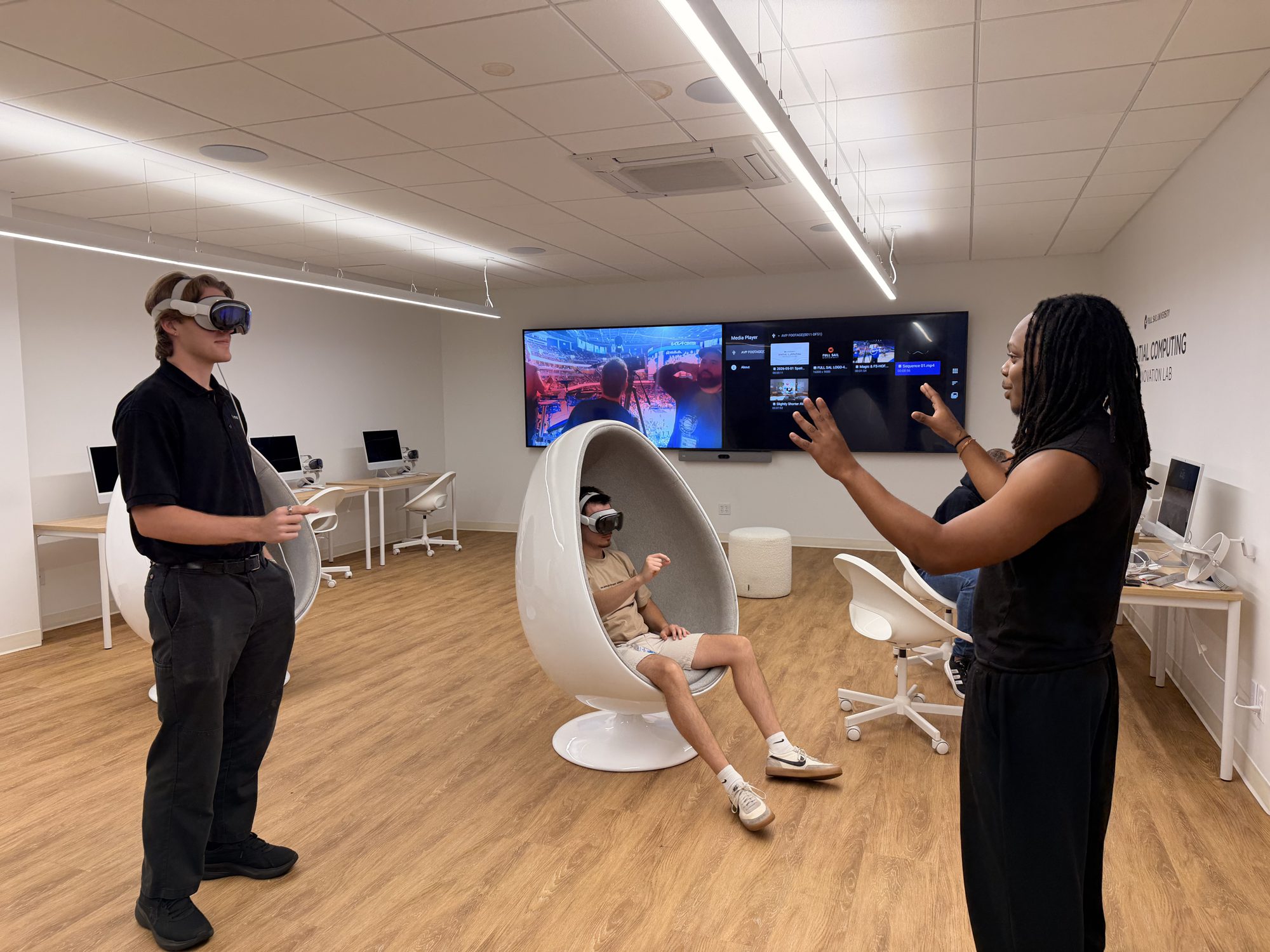 A student wearing Apple Vision Pro in the Spatial Computing Innovation Lab while another person demonstrates on the wall screen